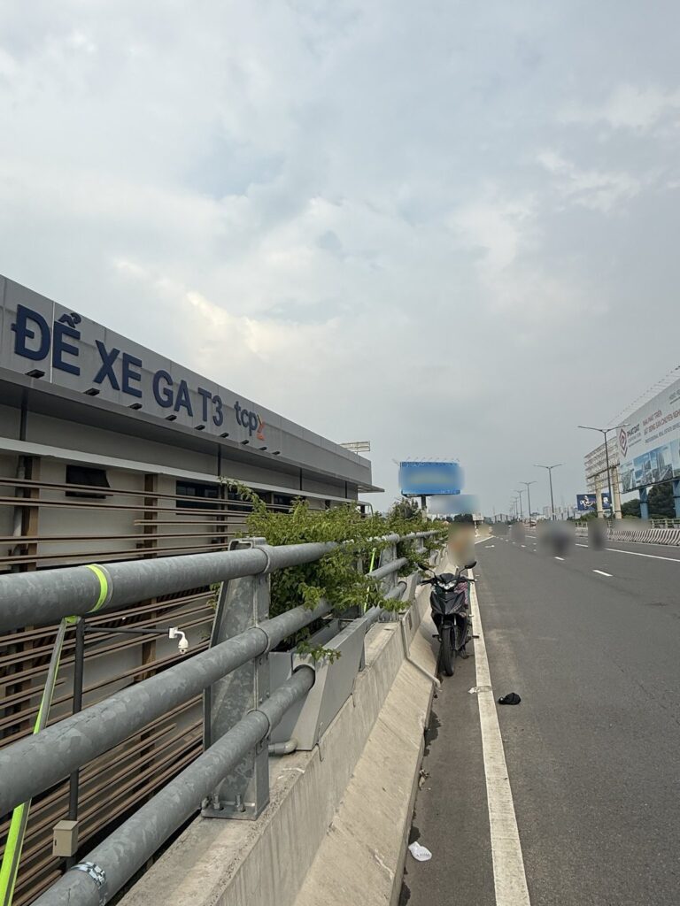 Đoạn đường trên cao cạnh bãi để xe Ga T3 sân bay Tân Sơn Nhất, lan can thép có bồn cây, người đi xe máy phía xa đã được làm mờ