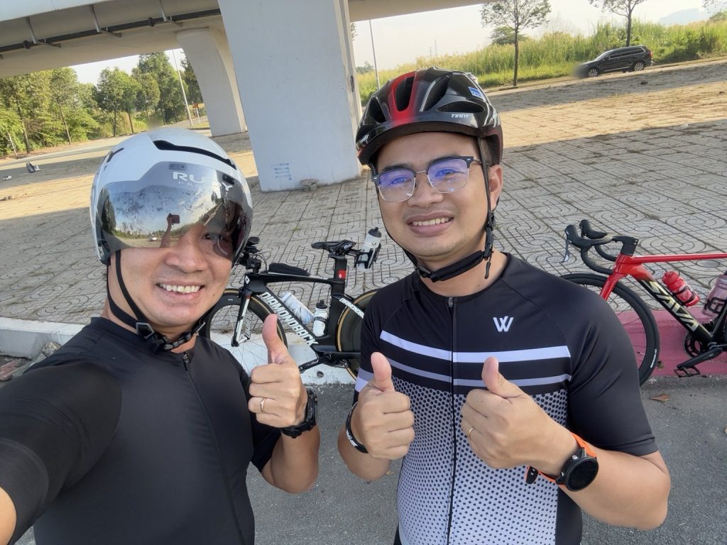 Tony Hoàn và Lê Tấn Đào đội mũ bảo hiểm, giơ ngón tay cái cạnh hai chiếc xe đạp